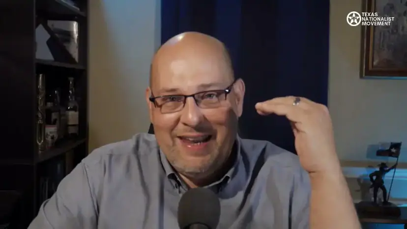 A smiling bald man in glasses gestures during a livestream from a home office.