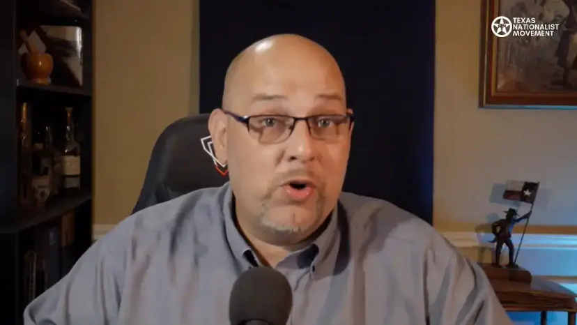 A bald man in glasses speaks to the camera during a livestream from a home office.