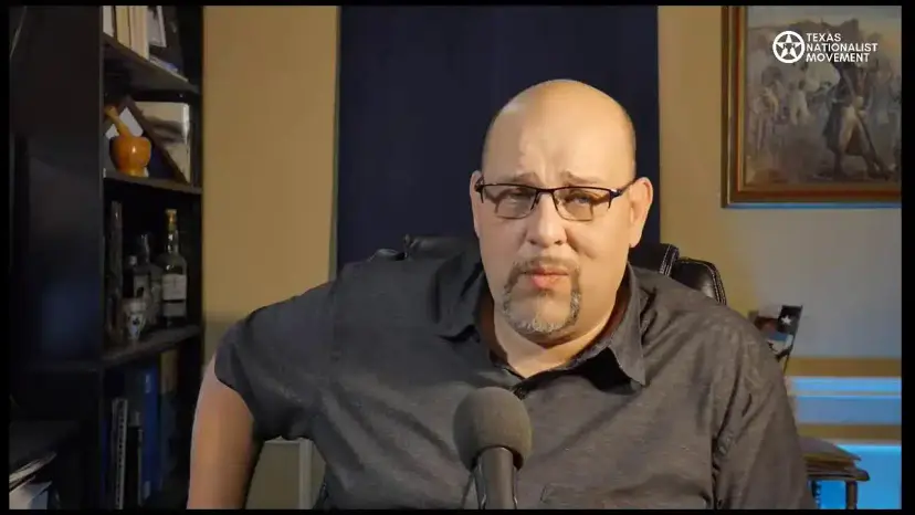 A bald man in glasses and a dark shirt looks at the camera during a livestream.
