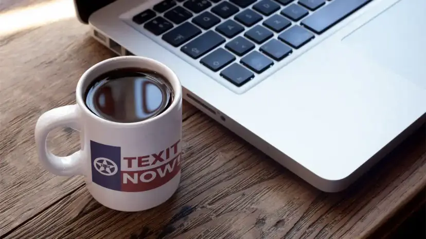 A white 'TEXIT Now' mug filled with coffee sits next to a silver laptop keyboard.