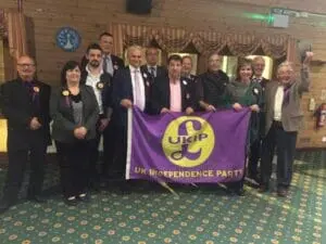 A group of people stand indoors holding a purple UK Independence Party banner.