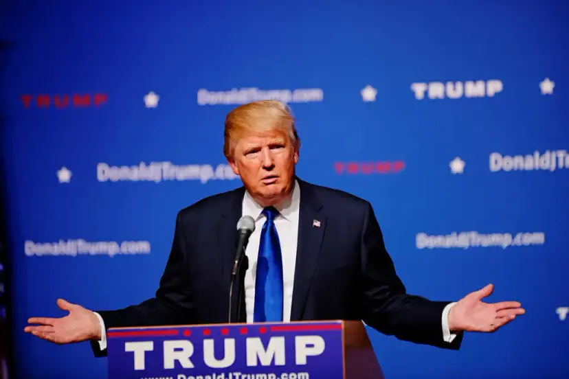 Donald Trump shrugging with arms spread at a podium reading "Trump" in front of a campaign backdrop.