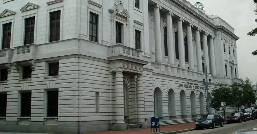 A large white stone courthouse with tall columns and arched windows on a street lined with parked cars.