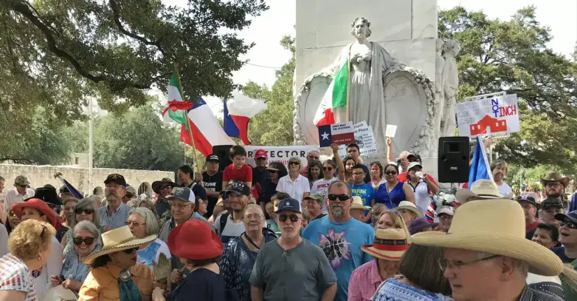 A large crowd with Texas flags and signs rallying in front of the Alamo Cenotaph in San Antonio.