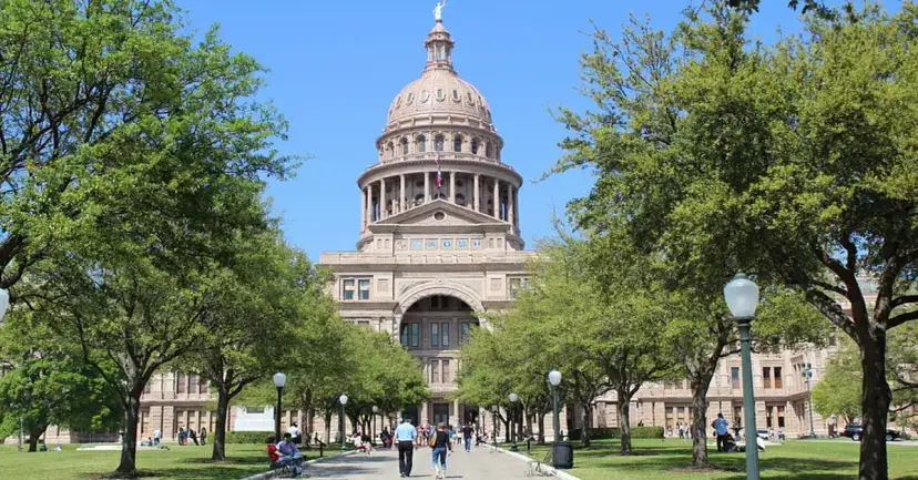 The Texas State Capitol and its dome, seen down a tree-lined walkway on a sunny day.