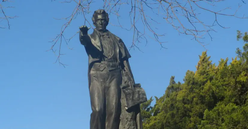 Bronze statue of Stephen F. Austin with an outstretched arm against a blue sky and trees.