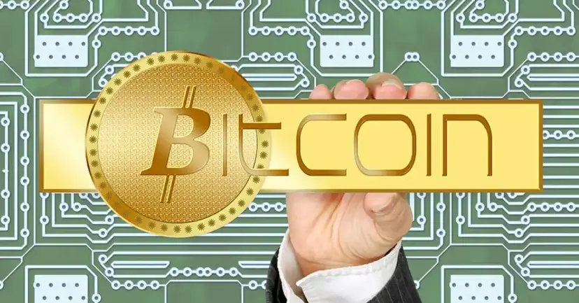 A hand holding a gold Bitcoin coin and a gold "Bitcoin" banner over a green circuit board pattern.