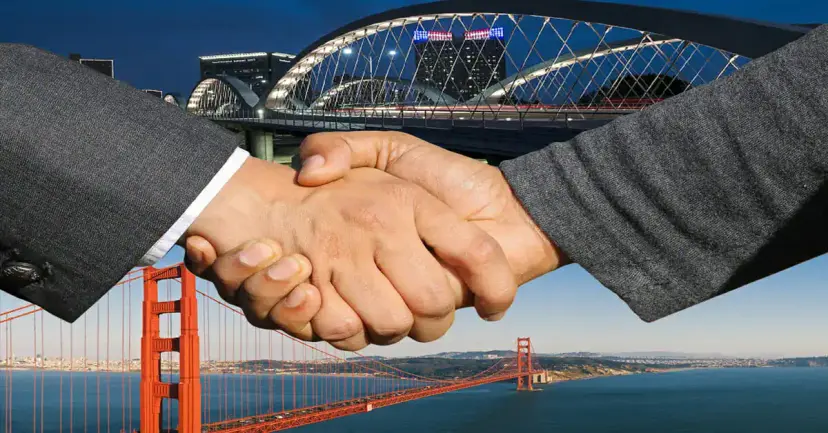 Two men in suits shaking hands in front of the Golden Gate Bridge and a lit arched bridge.
