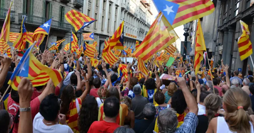 Large crowd waving Catalan independence flags on a city street lined with tall buildings.