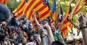 A crowd of demonstrators waving Catalan independence flags and raising their fists.