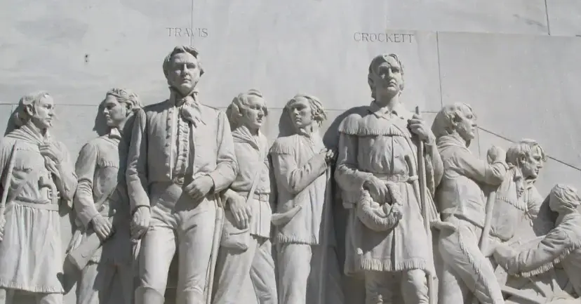 Carved relief of Alamo defenders on the Alamo Cenotaph, with the names Travis and Crockett above their figures.