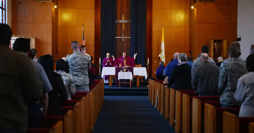 Congregation standing in wooden pews during a church service, several people in military uniforms.