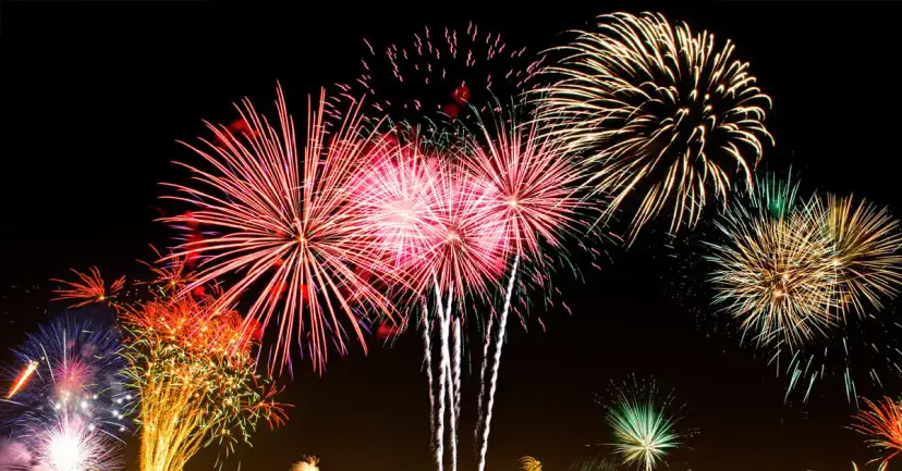 Bursts of pink, gold, orange, and green fireworks against a black night sky.