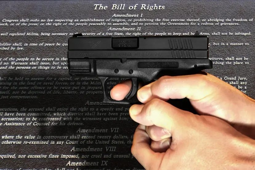 Hand holding a black handgun over a printed copy of the Bill of Rights.