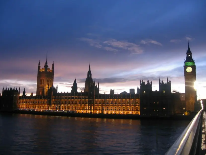 Houses of Parliament and the Big Ben clock tower lit up at sunset along the River Thames.