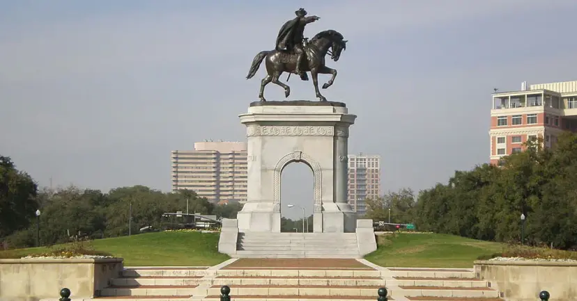 Equestrian statue of Sam Houston atop a stone arch in a Houston park, with buildings behind.