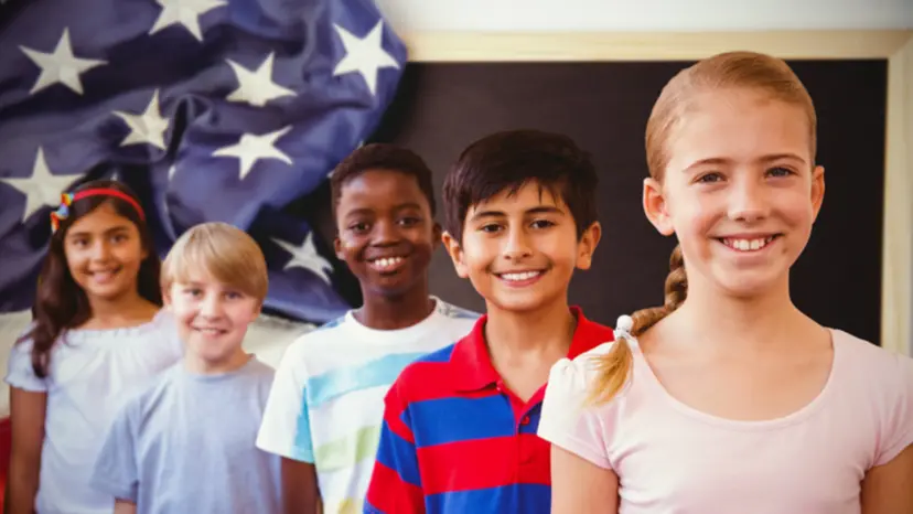 Five smiling schoolchildren standing in a row in front of an American flag in a classroom.