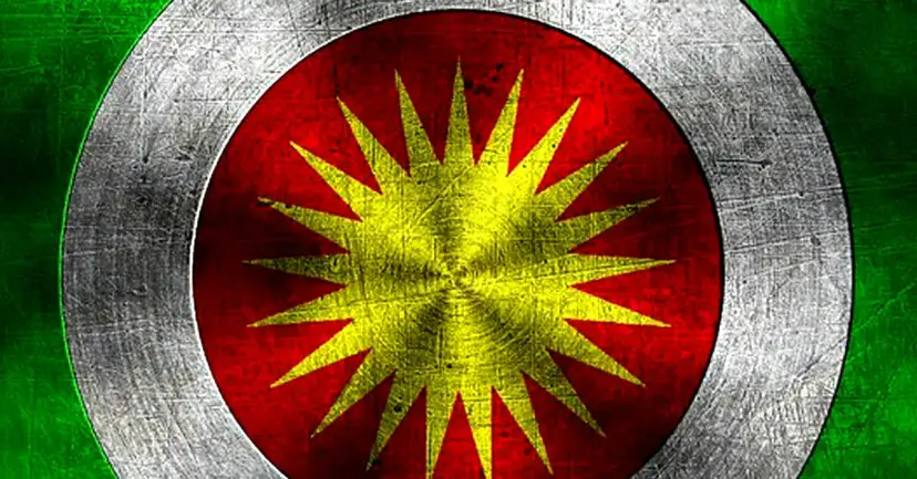 Stylized Kurdish sun emblem, a yellow sunburst on red ringed by white and green, with a scratched texture.
