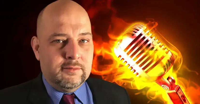 Daniel Miller in a suit and tie beside a vintage studio microphone engulfed in flames.