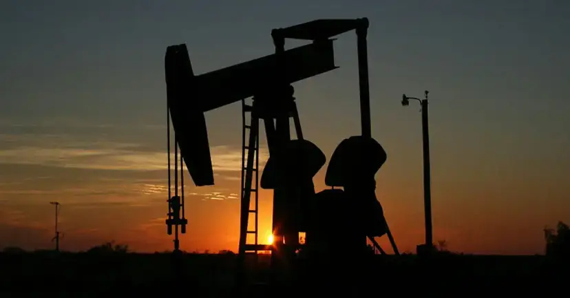 Silhouette of an oil pumpjack against an orange sunset sky.