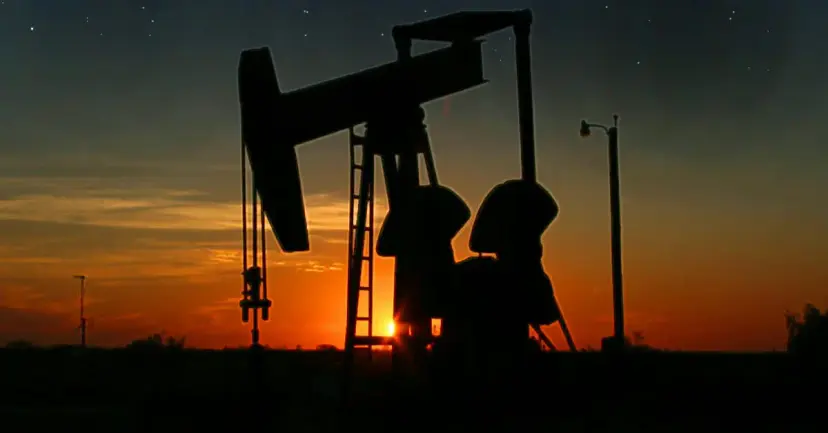 An oil pump jack silhouetted against an orange sunset.