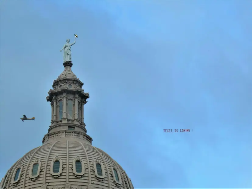 Plane pulling a 'TEXIT is coming' banner across the sky beside the statue atop the Texas Capitol dome.