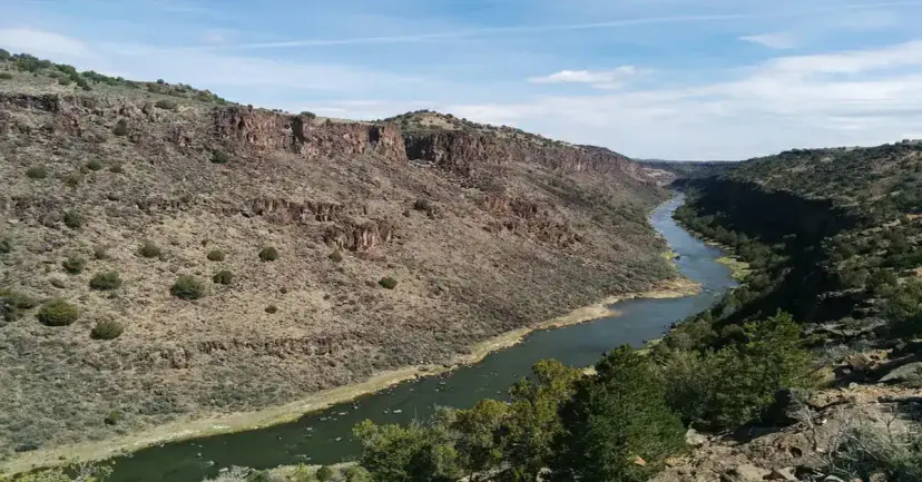 A river winding through a rocky, brush-covered canyon under a blue sky with scattered clouds.