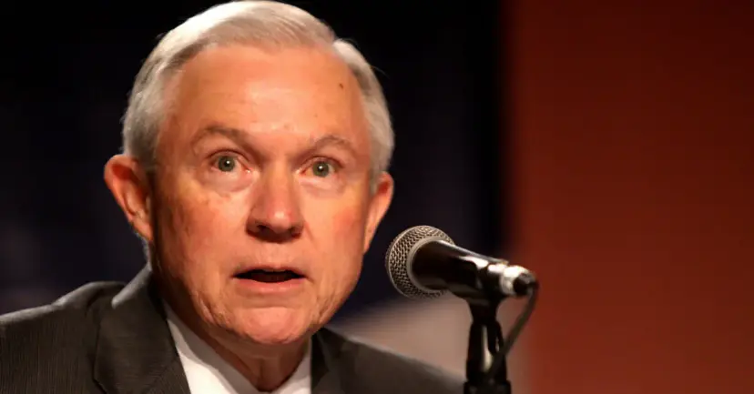 Attorney General Jeff Sessions speaking at a microphone against a dark background.