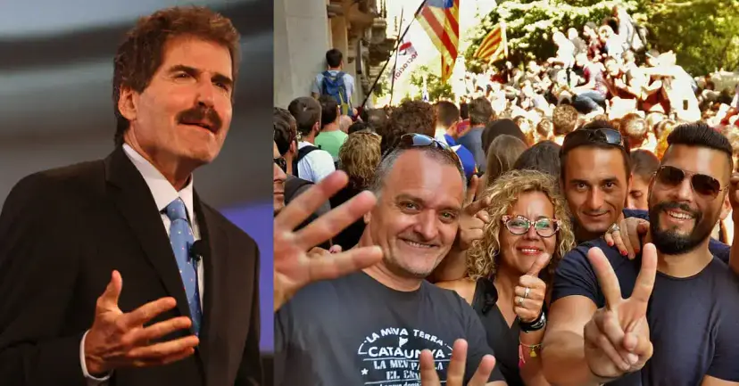 John Stossel speaking on stage beside a crowd of smiling Catalan independence supporters flashing peace signs.