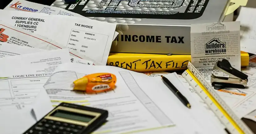 Tax paperwork, an income tax binder, a calculator, a pen and a ruler spread across a desk.