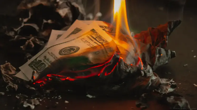 U.S. dollar bills burning in a pile of charred paper.