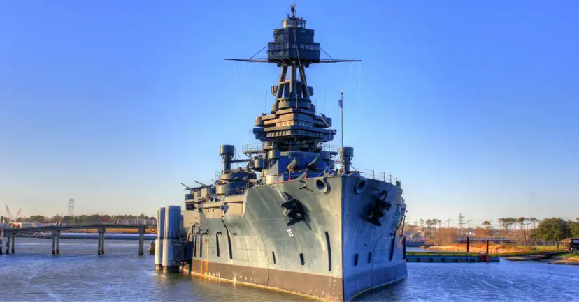 The battleship USS Texas moored on calm water under a clear blue sky.