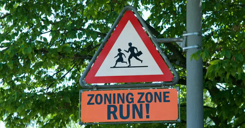 Red triangle road sign with running figures above an orange sign reading "Zoning Zone Run!"