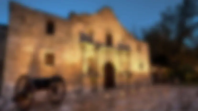 Blurred photo of the Alamo at dusk with a cannon in front.