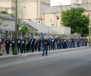 Long line of people in matching navy shirts standing along a downtown street near historic buildings.