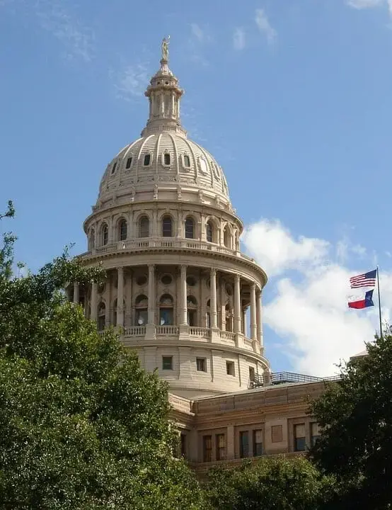 Dome of the Texas State Capitol with the American and Texas flags flying against a blue sky.