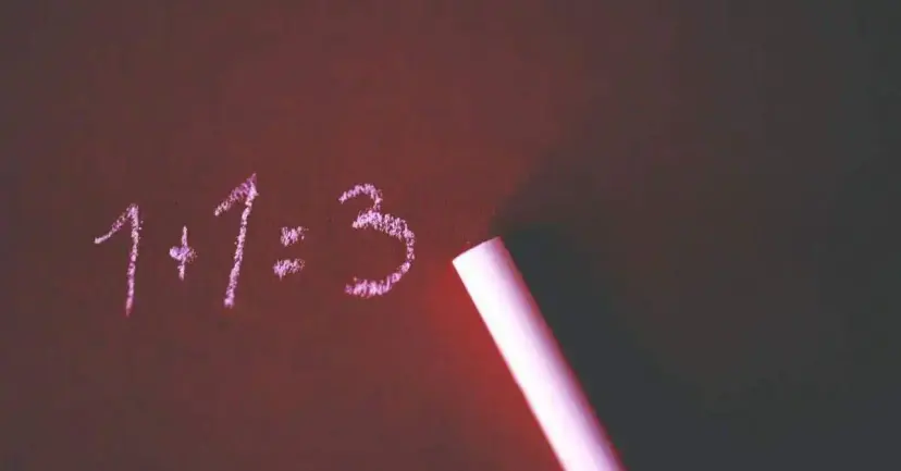 The equation '1+1=3' written in chalk on a chalkboard beside a piece of chalk.