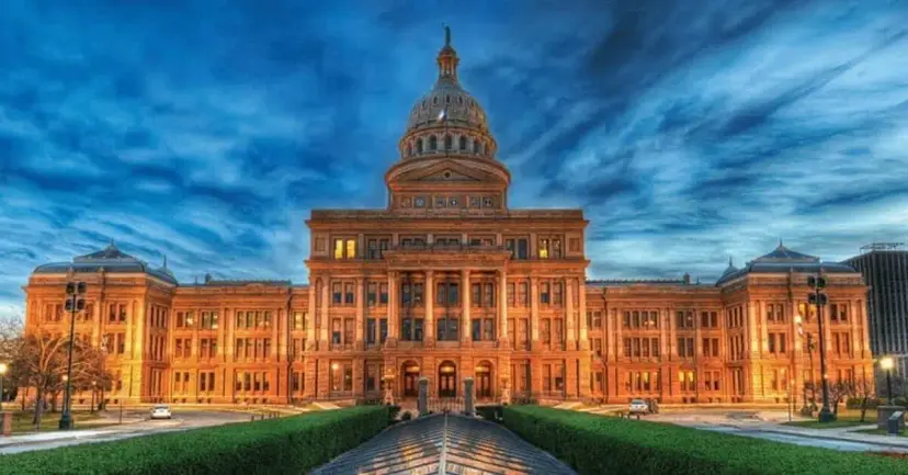 The Texas State Capitol at dusk, glowing in warm light under a dramatic blue sky.