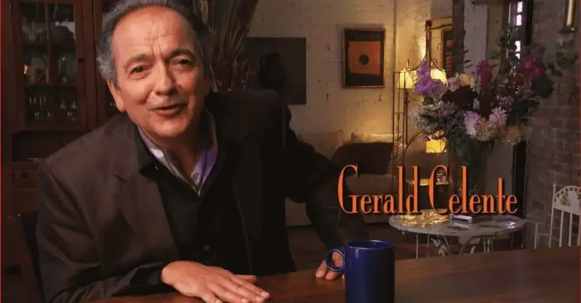 Gerald Celente, named on screen, seated at a table in a warmly lit living room with a coffee mug.