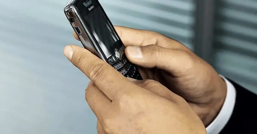 Close view of hands holding an older smartphone with a physical keyboard.