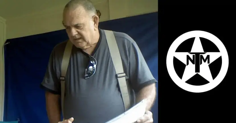 An older man in suspenders and a gray shirt reading papers, beside the white TNM star logo.