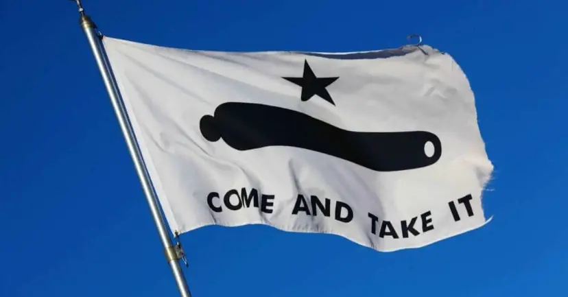 A white 'Come and Take It' flag with a black cannon and star flying against a clear blue sky.
