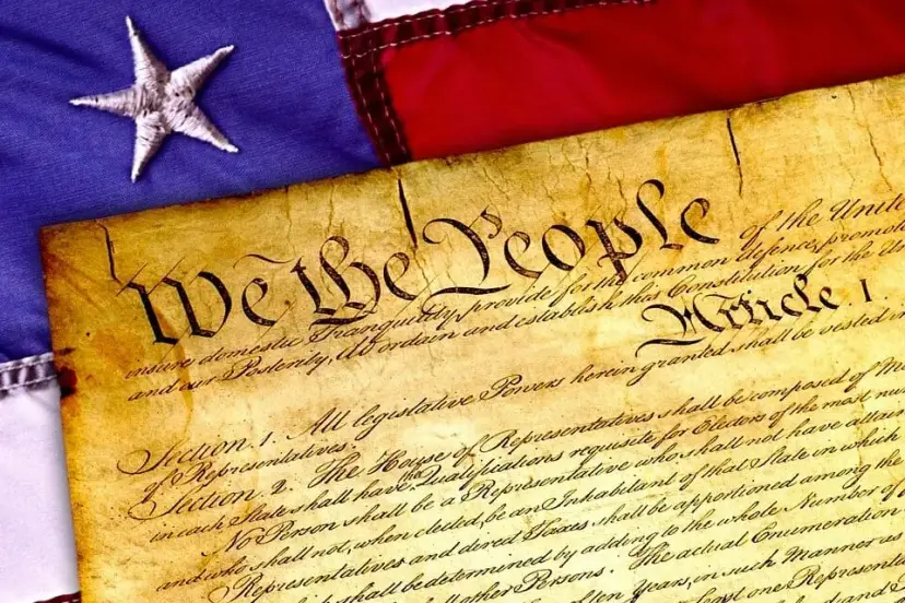Aged parchment of the Constitution opening with "We the People" resting on an American flag.