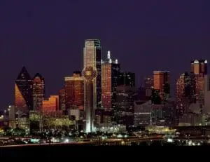 The downtown Dallas skyline lit up at night over dark ground.