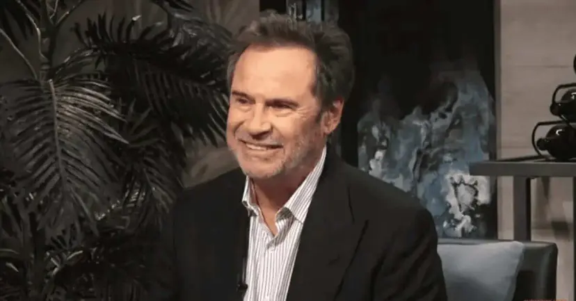Comedian Dennis Miller smiling in a dark jacket and striped shirt in a studio setting.