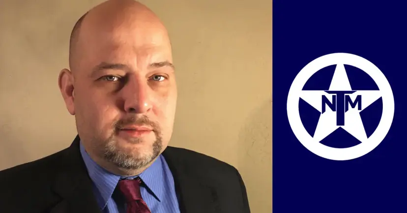 Portrait of a bald, bearded man in a suit and red tie beside the white TNM star logo on navy.