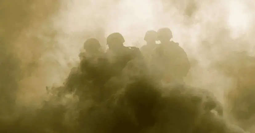 Silhouetted soldiers moving through thick clouds of smoke and dust.