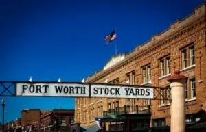 Fort Worth Stock Yards sign arching over a street in front of a brick building flying a flag.