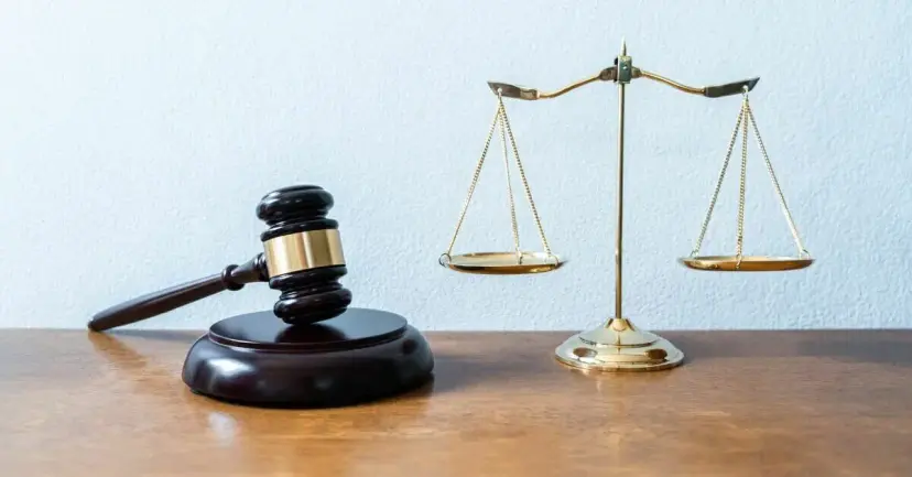 A judge's gavel on a wooden desk beside a brass scale of justice.