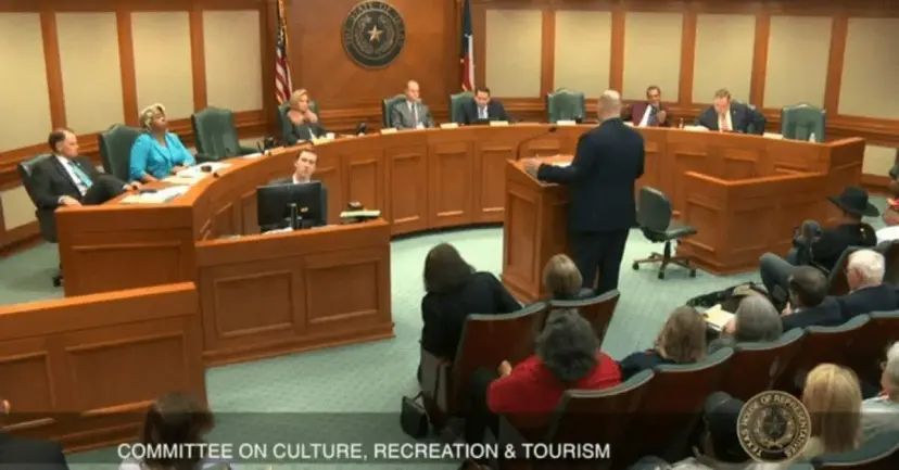 A man testifies at a lectern before the Texas House Committee on Culture, Recreation and Tourism in a hearing room.